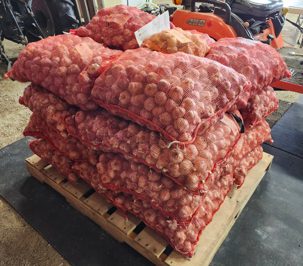 Stack of bags containing garlic on a wooden pallet with a tractor in the background.