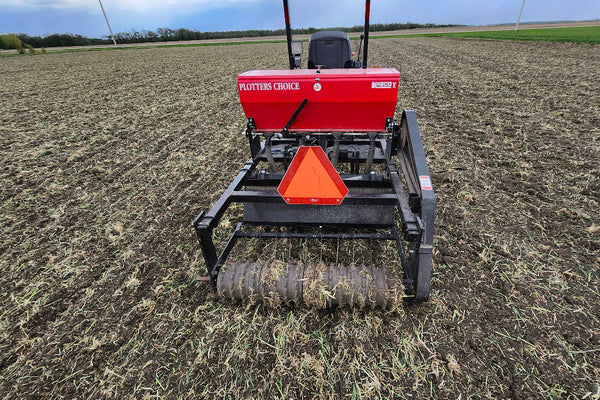 Small tractor on a field with a red seeder planting a crop